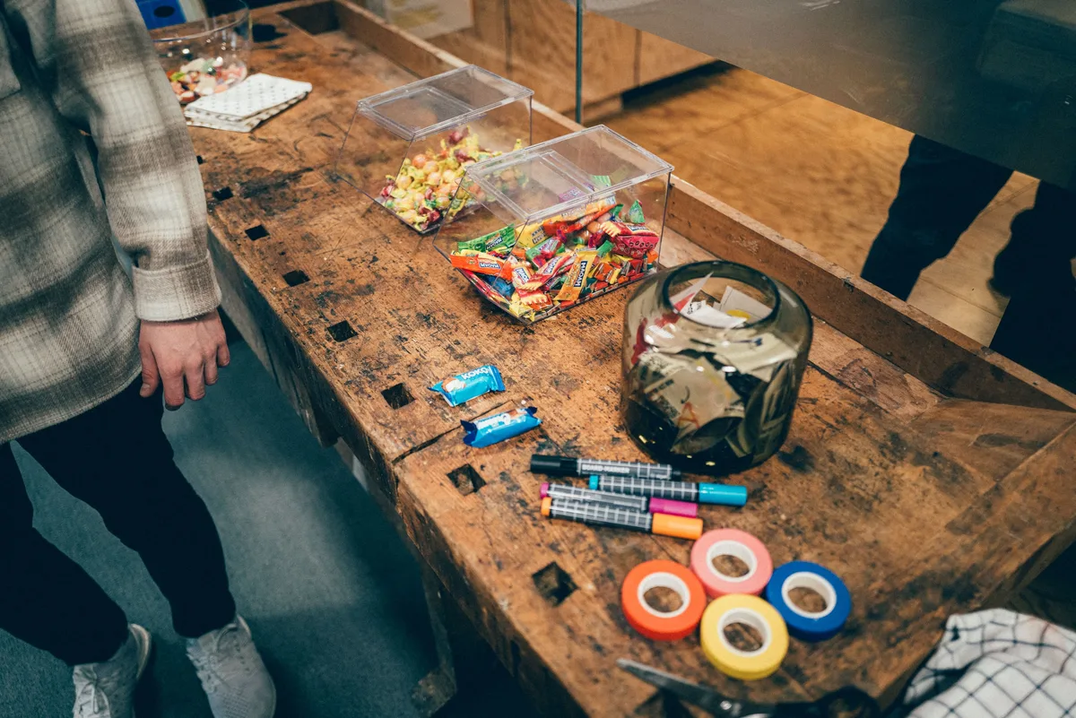 Süßigkeiten in Plastikboxen, bunte Klebebänder und Filzstifte liegen auf einer alten Werkbank