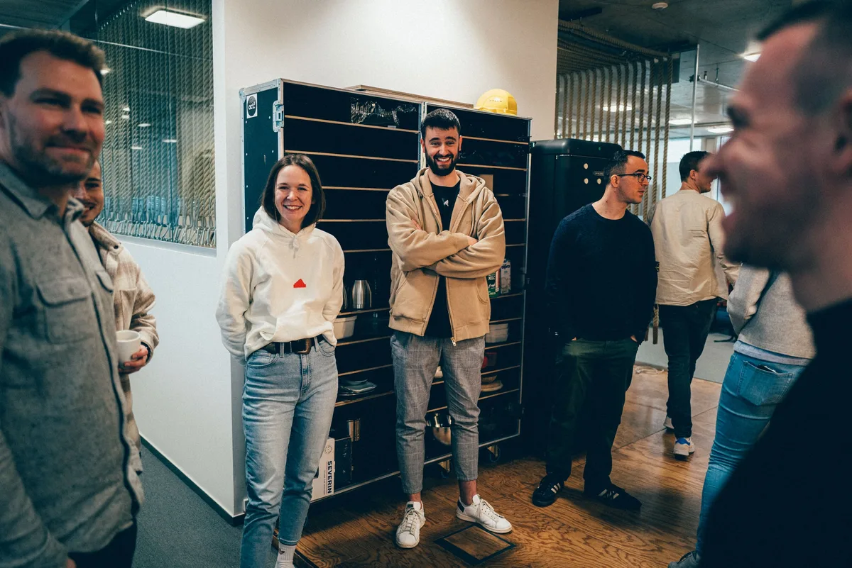 Gruppe lächelt vor einem Flightcase-Regal, darunter eine Frau im weißen Hoodie und ein Mann mit verschränkten Armen