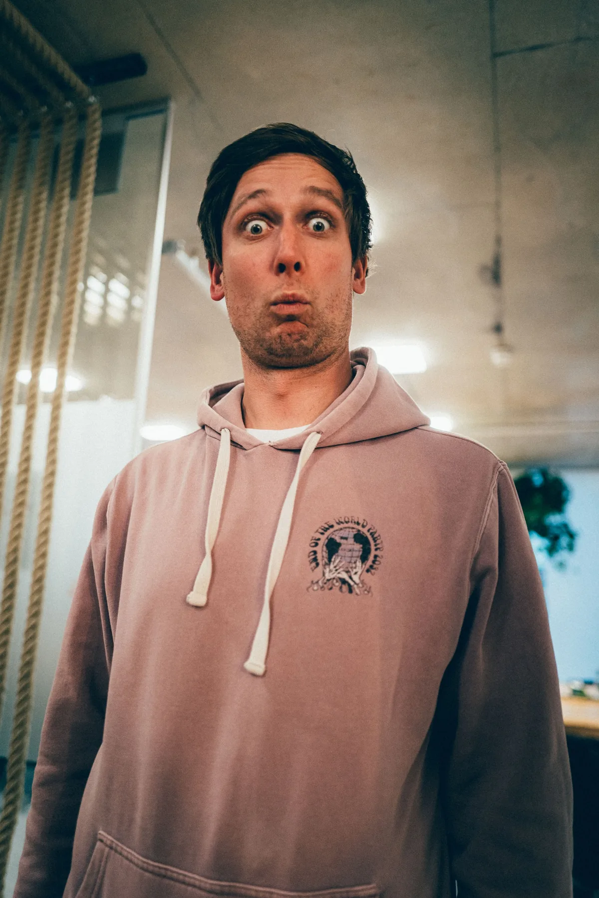 Mann im rosa Hoodie reißt die Augen auf und zieht die Lippen zusammen, links hängen dicke Seile