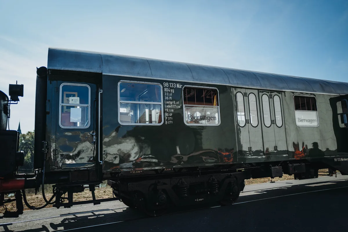 Dunkelgrüner Personenwagen mit der Aufschrift „Bierwagen“ im Seitenlicht, links das Ende der Lok