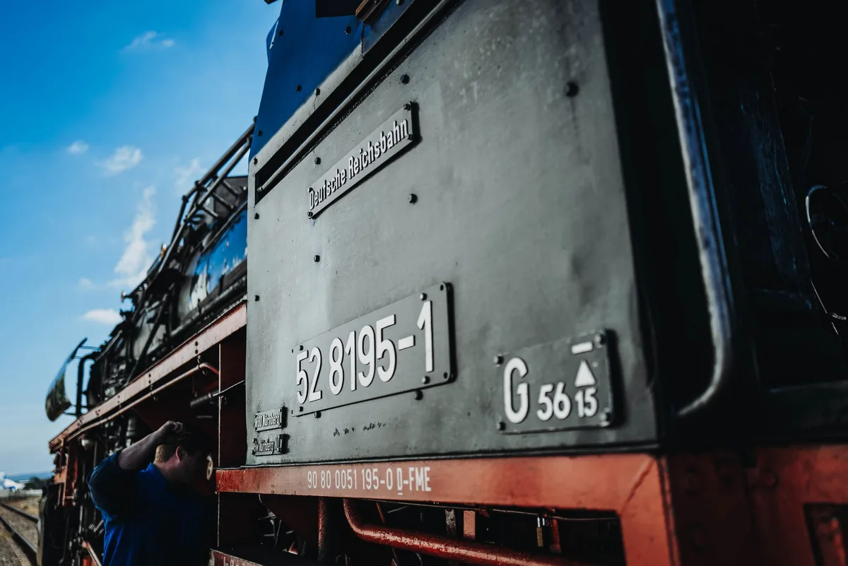 Schilder „Deutsche Reichsbahn“ und „52 8195-1“ am Führerhaus der Lok, unten links ein Mann mit erhobenem Arm