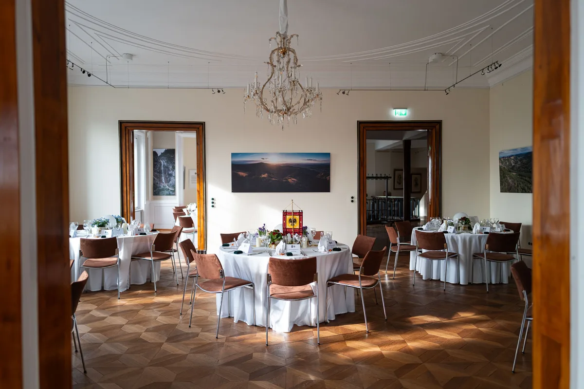 Blick durch zwei Türrahmen in den eingedeckten Saal, Kronleuchter und Sonnenlicht auf dem Rautenparkett