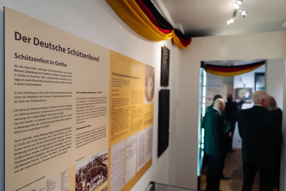 Ausstellungstafel zur Gründung des Schützenbundes in Gotha, hinten Gäste im Gang, darüber ein schwarz-rot-goldener Stoff