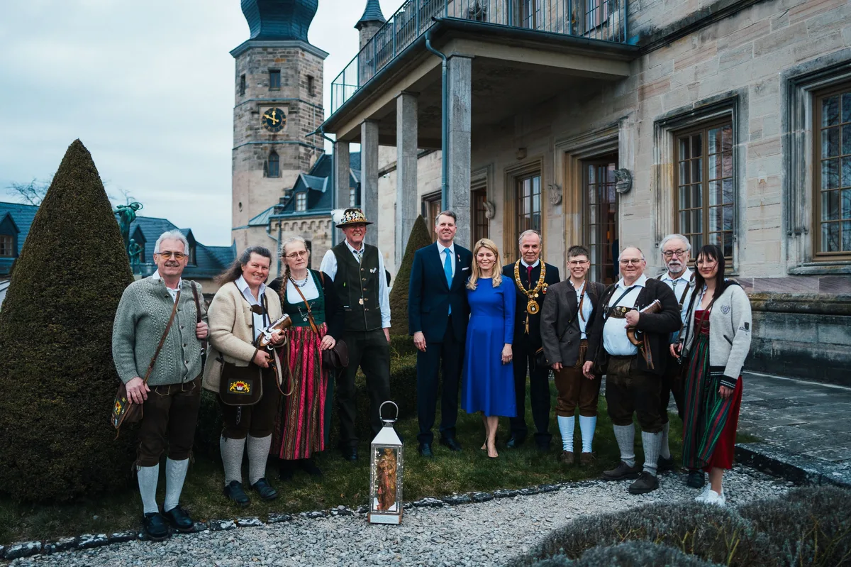 Gruppenbild im Garten: Menschen in Tracht, ein Mann im Anzug, eine Frau im blauen Kleid und ein Mann mit Amtskette