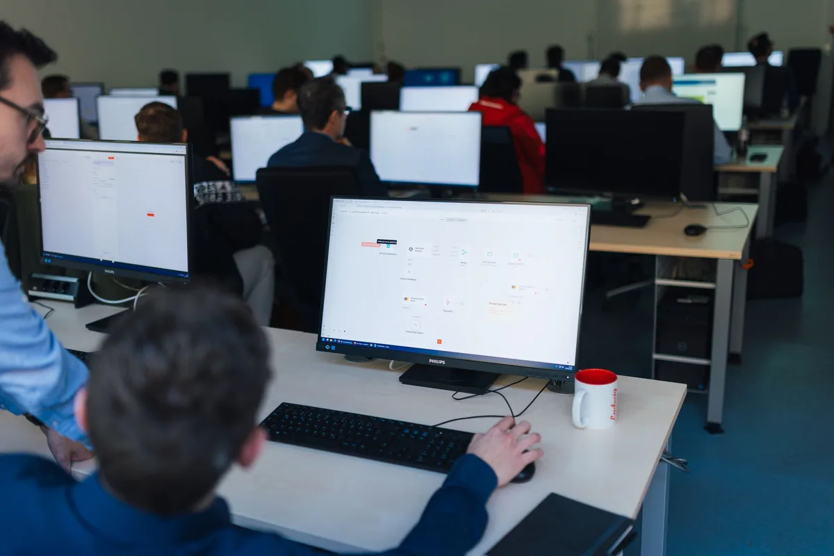 Hinterkopf eines Teilnehmers vor einem Monitor mit Workflow-Diagramm, daneben ein Becher mit rotem Aufdruck