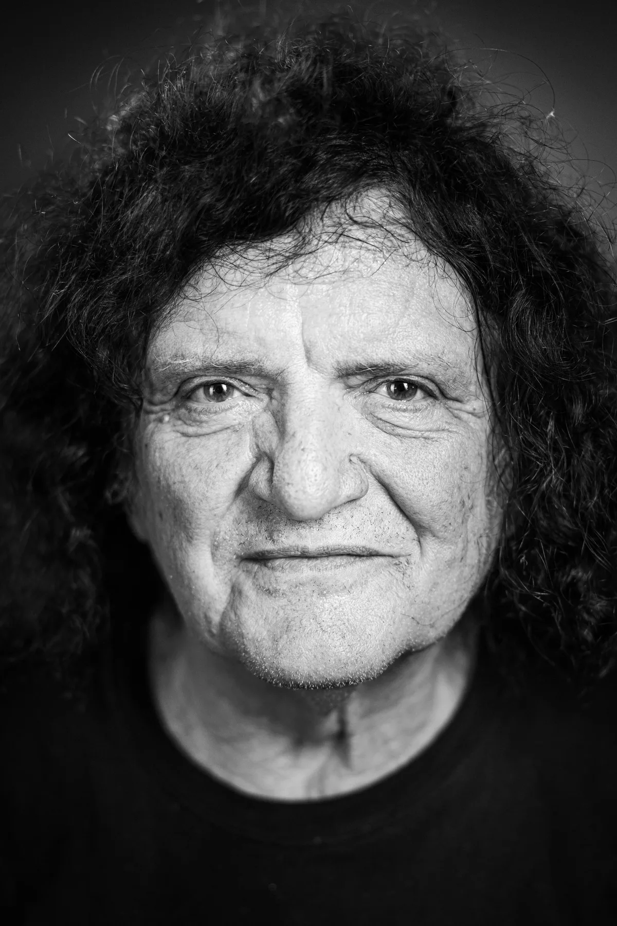 Mann mit dichten dunklen Locken und schwarzem Shirt blickt mit leichtem Lächeln in die Kamera