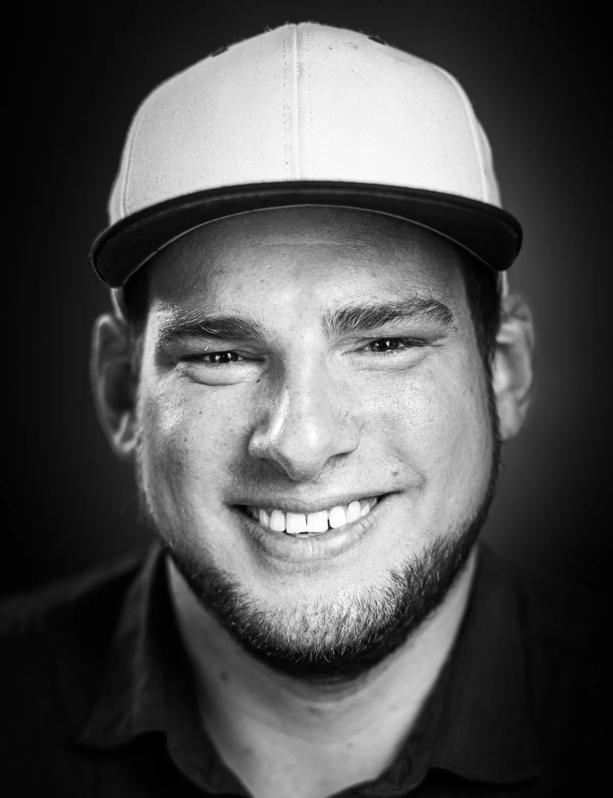 Lachender junger Mann mit heller Snapback-Cap, Kinnbart und dunklem Hemd