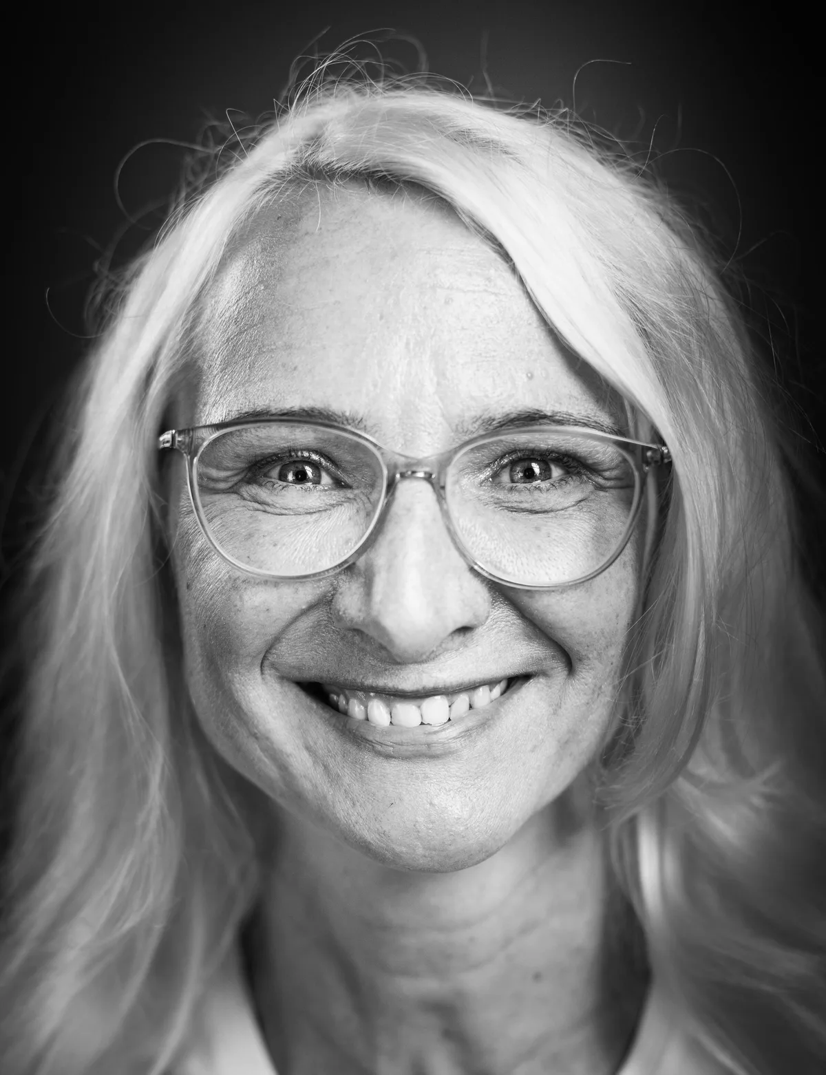 Lächelnde Frau mit langen hellblonden Haaren und transparenter Brille, ganz nah am Gesicht fotografiert