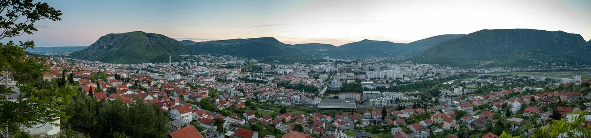 Panorama einer Stadt im Talkessel mit roten Dächern und Hochhäusern, dahinter Bergketten in der Dämmerung