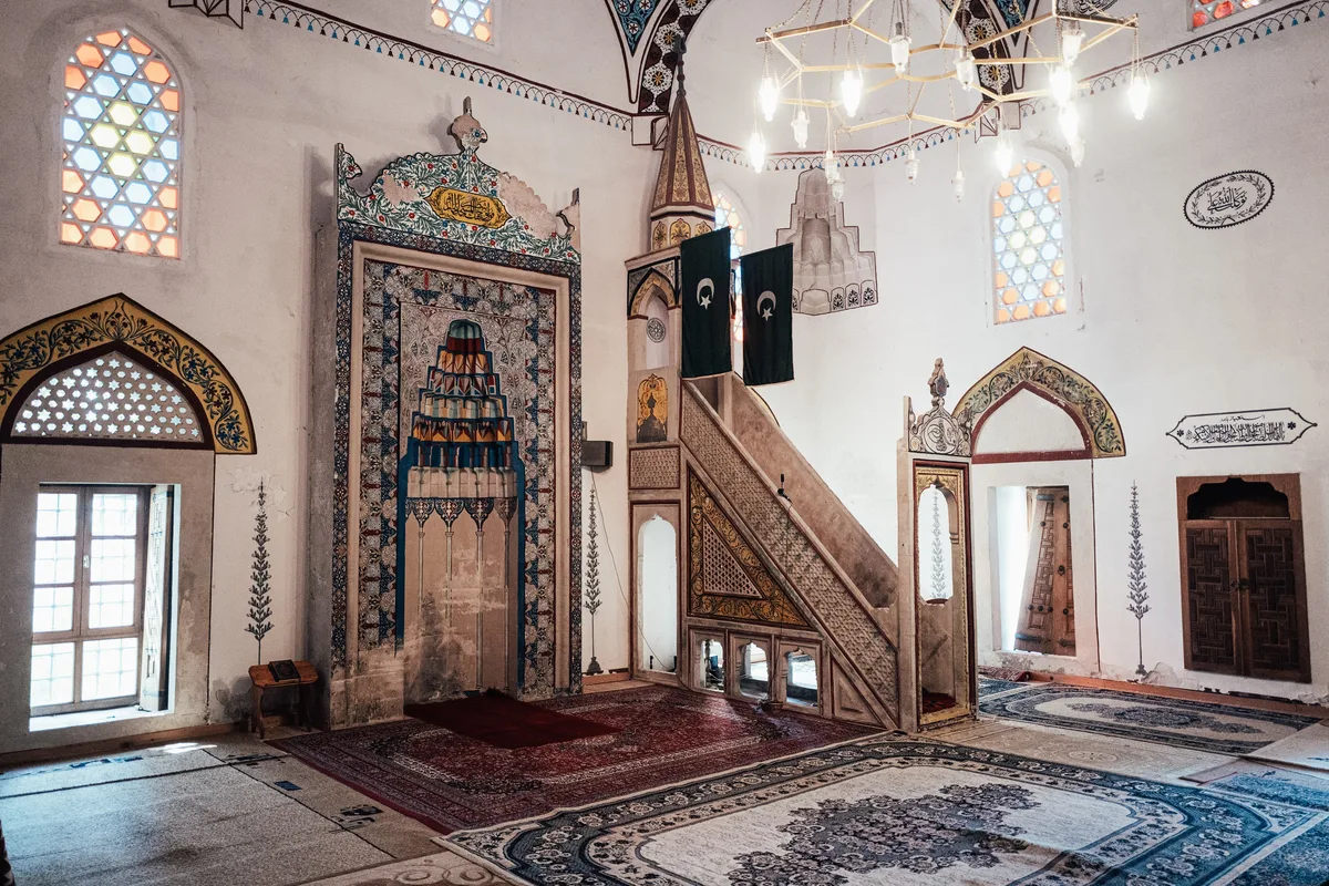 Innenraum einer Moschee mit Gebetsnische, Kanzel, bunten Fenstern, Kronleuchter und gemusterten Teppichen