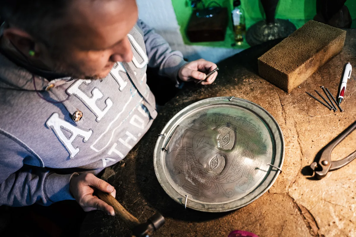 Von oben auf den Mann an der Werkbank, der mit Hammer und Stichel ein Gesicht in eine runde Metallschale arbeitet