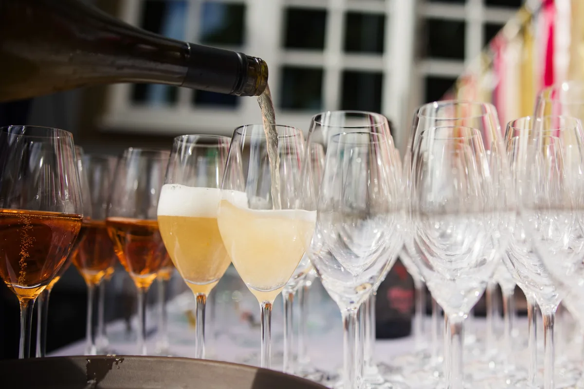 Aus einer Flasche wird Schaumwein in Gläser gegossen, links stehen schon gefüllte Gläser, rechts leere