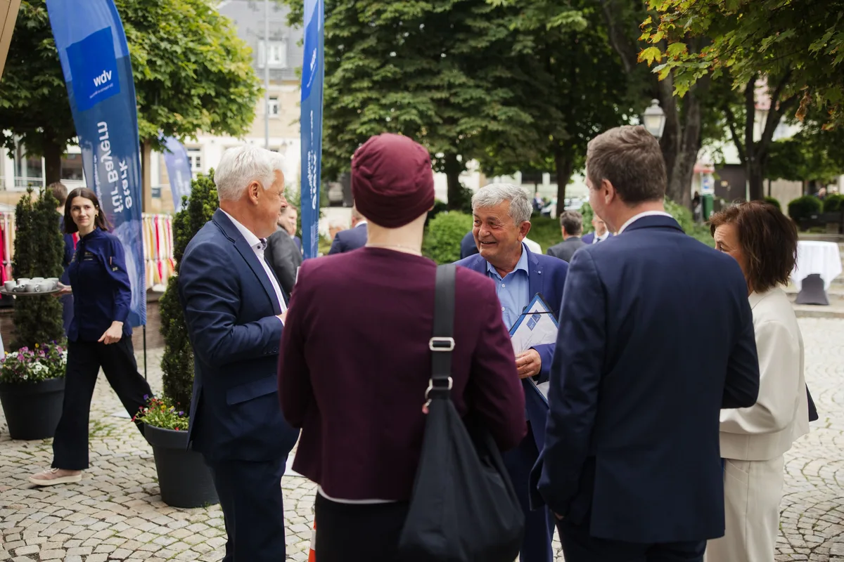 Gesprächsrunde auf dem Marktplatz, vorn eine Frau mit bordeauxroter Mütze von hinten, dahinter ein lachender älterer Mann