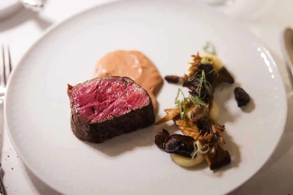 Rosa gebratenes Rindfleisch auf weißem Teller mit Pilzen, Kartoffelpüree und heller Sauce, links eine Gabel