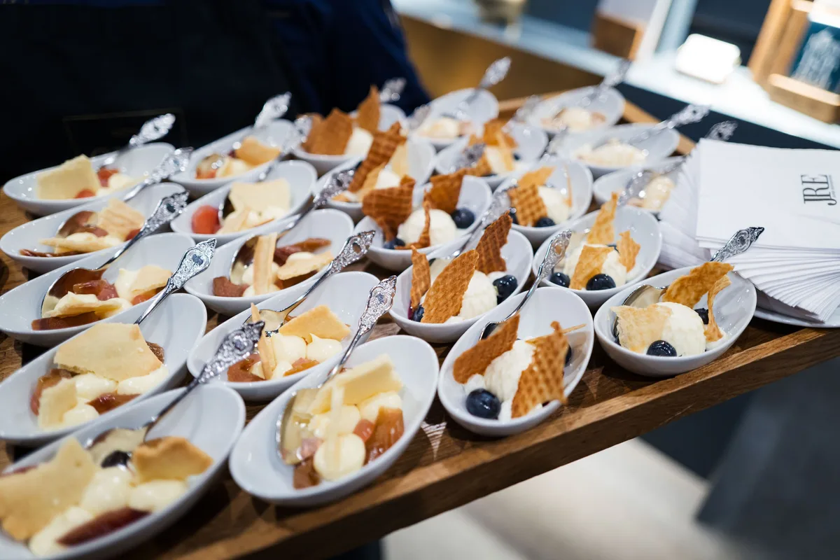 Holztablett mit zahlreichen weißen Schälchen, darin Eiscreme, Heidelbeeren und Waffelstücke, jeweils mit verziertem Löffel