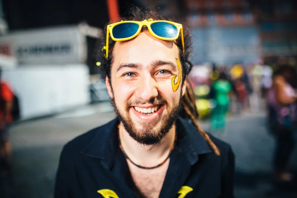 Nahaufnahme eines lächelnden Mannes mit Bart, gelber Sonnenbrille auf der Stirn und gelbem Zeichen auf der Wange
