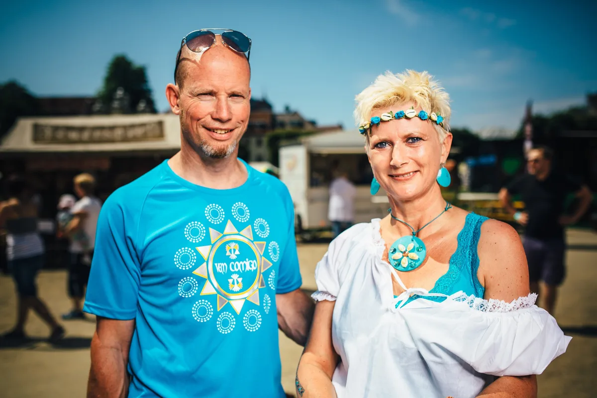 Querformat-Porträt: Mann mit Sonnenbrille im Haar und Frau mit türkisem Schmuck lächeln in die Sonne