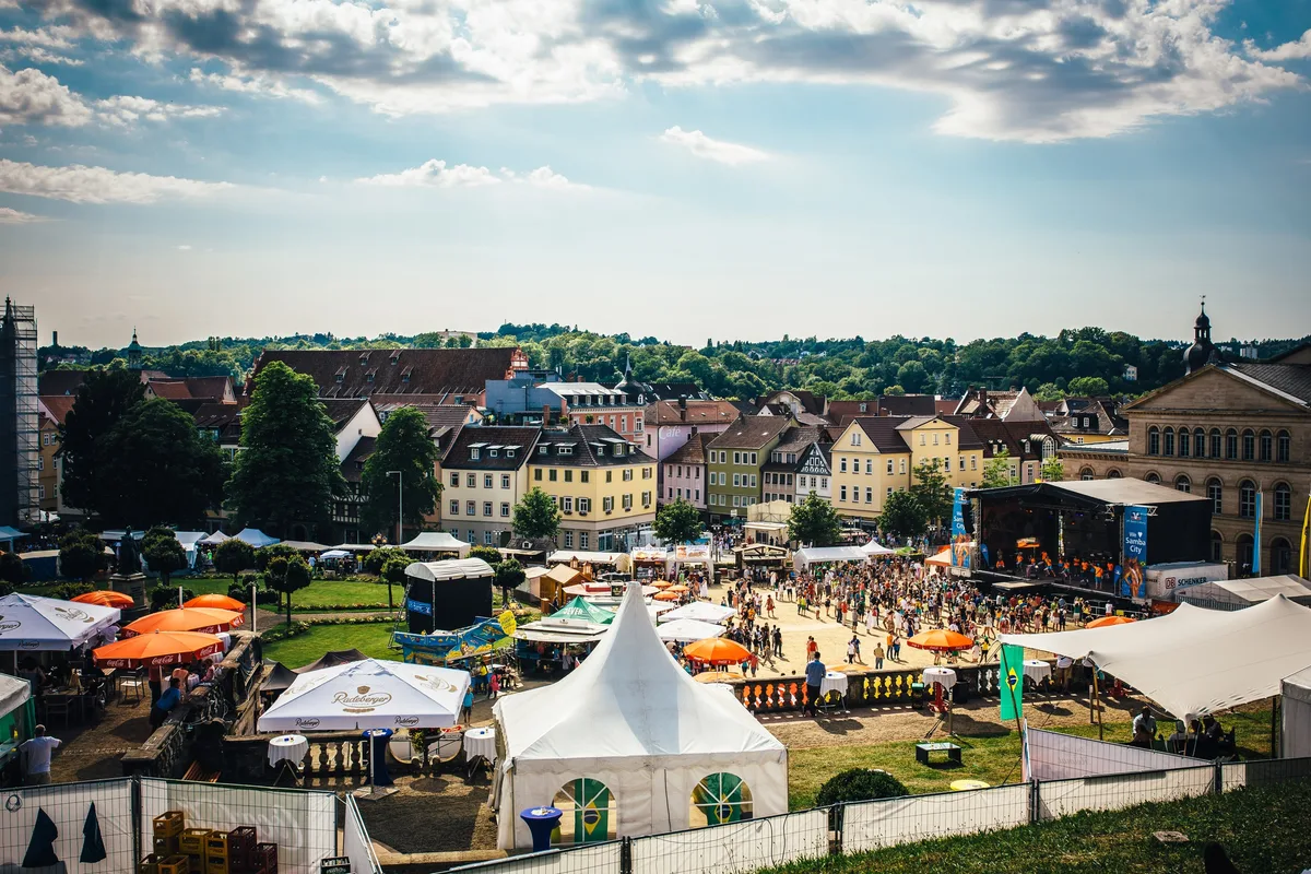 Überblick über den Festivalplatz mit Zelten, Bühne und Menschenmenge zwischen Altstadthäusern und bewaldeten Hügeln