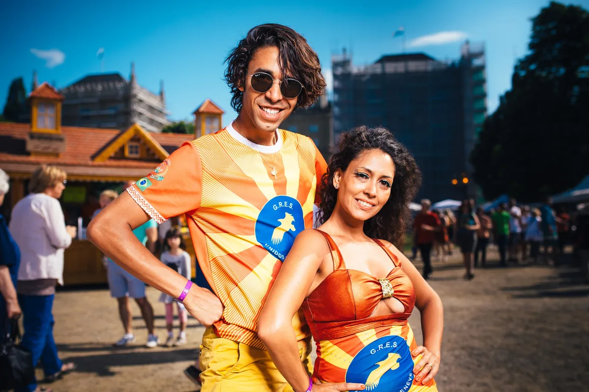 Enges Porträt des Paares in orange-gelben Trikots, er mit Sonnenbrille und Armband, sie mit lockigem Haar