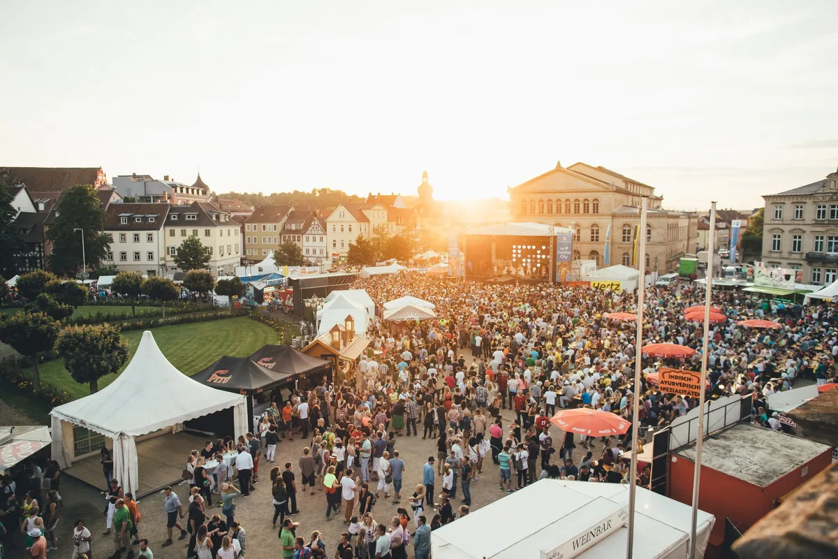 Blick von oben auf Bühne und dichtes Publikum bei Sonnenuntergang, Zelte und Dächer der Altstadt dahinter