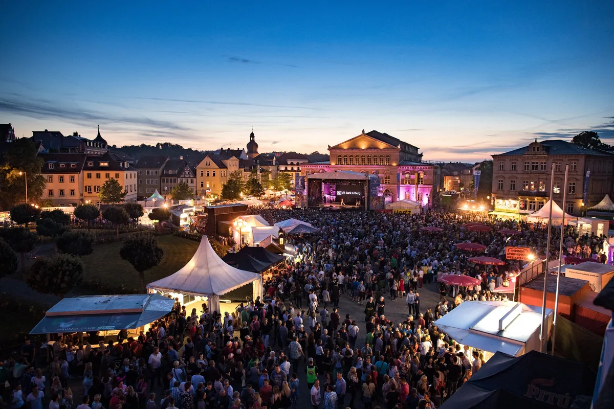 Festplatz mit Bühne und Menschenmenge in der blauen Stunde, Dächer der Altstadt und Zelte im Abendlicht