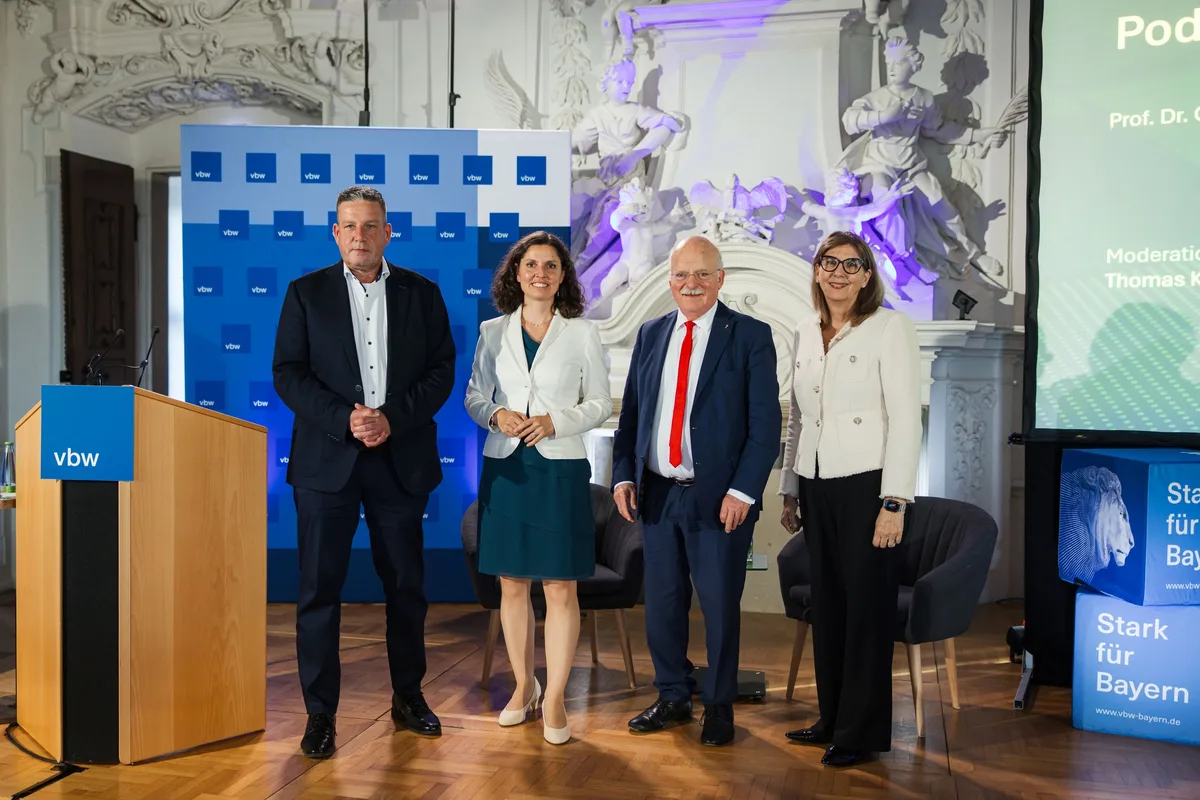 Zwei Männer und zwei Frauen stehen für ein Gruppenfoto auf dem Parkett vor dem Pult, hinten die blaue Logowand