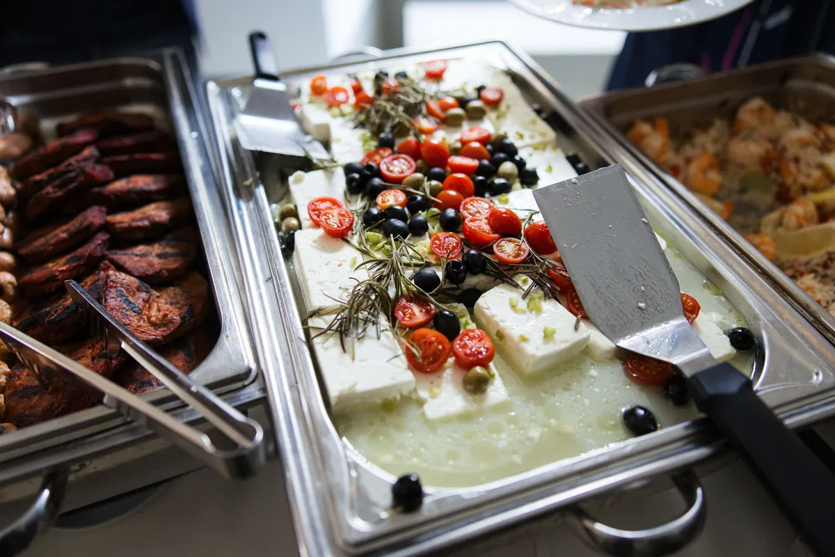 Wärmewanne mit Feta, Kirschtomaten, Oliven und Rosmarin, links Grillfleisch, rechts Reis mit Garnelen