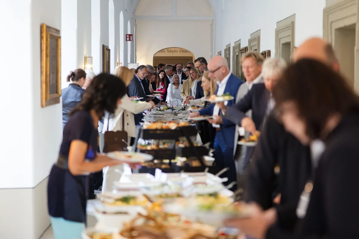 Tief angesetzter Blick über das Buffet auf Gäste, die im Gang mit Tellern anstehen, im Vordergrund Salate und Brot